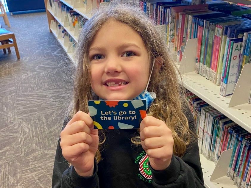 Child holding student library card that says let's go to the library