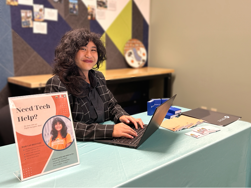 Woman with black hair wearing black and white blazer sitting at table with laptop