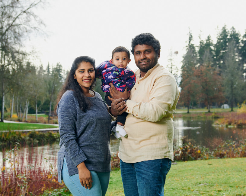 Family holding a baby standing outside on the grass in front of a pond